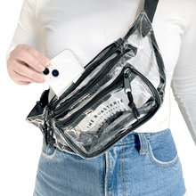 Load image into Gallery viewer, Person wearing Roasterie Clear Fanny Pack placing a white phone into one of the three zippered compartments