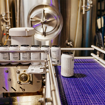 Image of a couple of a couple cold brew cans being sent down a conveyor belt. 