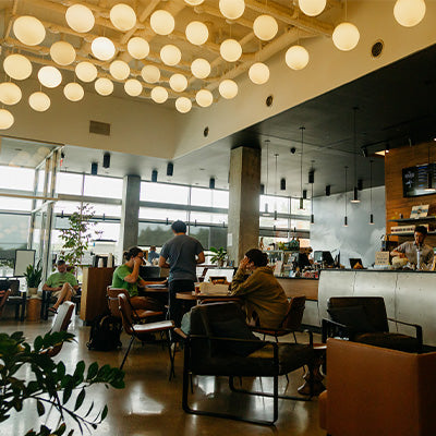 Image of the inside of the Woodside Cafe. 4 people are gathered inside conversing, working, and indulging in all of The Roasterie's cafe offerings.