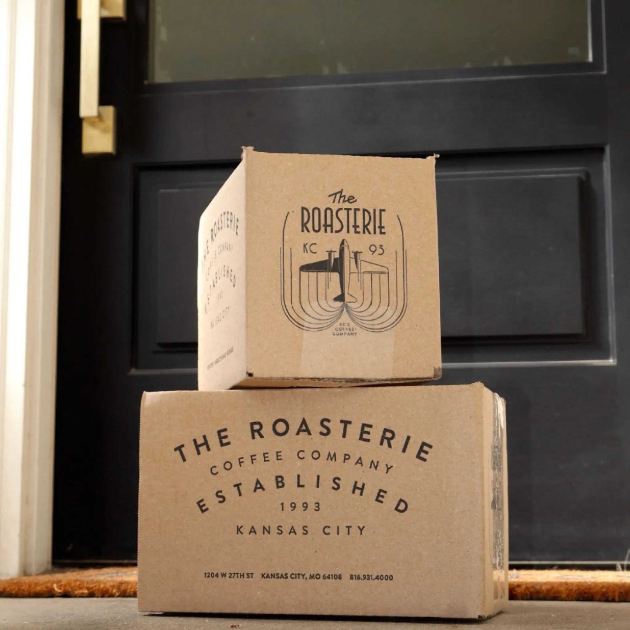 Two cardboard boxes from The Roasterie Coffee Company stacked in front of a door.