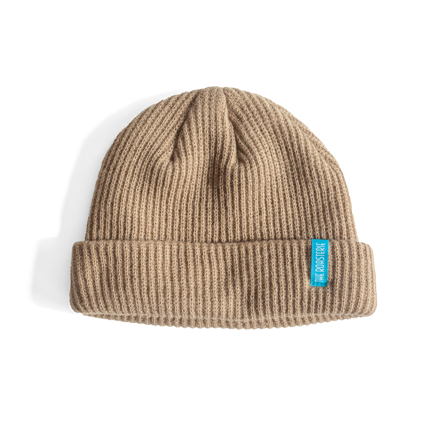 Dock Beanie in warm beige ribbed knit with folded cuff and small turquoise brand tag, photographed on white background showing classic winter hat design and textured knit pattern